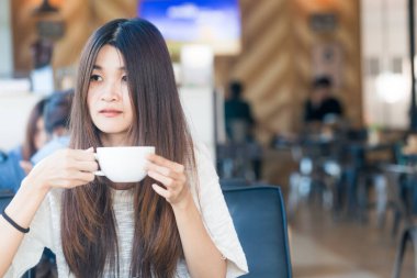 Asyalı öğrenci kadın çekici genç fincan kahve içecek kafe kitaplığında tutun.