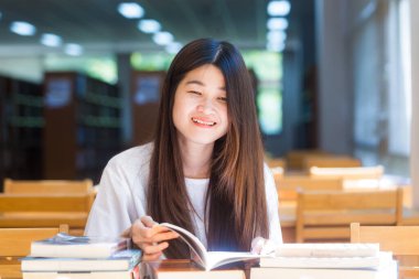 Kütüphanede bir kitap okumaya oturan genç çekici Asyalı kadın portresi. Eğitim kavramı