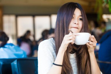 Bir fincan sütlü kahve Kütüphane arka plan iş hakkında düşünürken, onun elinde tutan öğrenci kadın