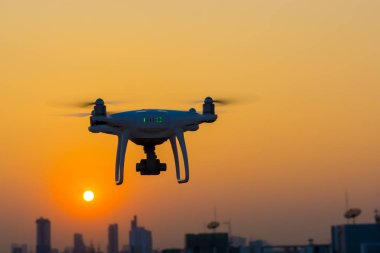 Gün batımında şehir binasında uçan siluet kuadkopter.