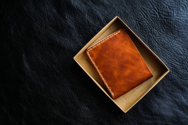 Siyah deri arka planda bitkisel bronzlaşmış deri cüzdan, işçilik objesi.