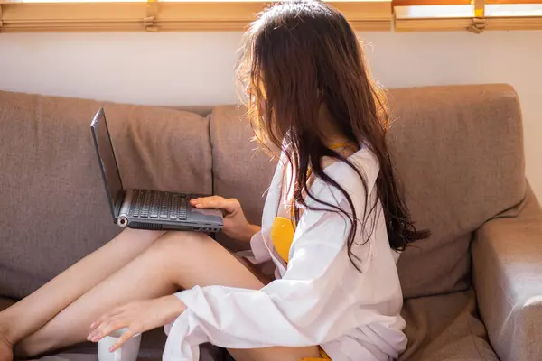 Business asian woman lying on sofa use laptop computer in cozy house morning wake up work from anywhere
