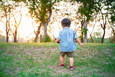 Neşeli çocuk Asyalı 2 yaşındaki çocuk şehir parkında oynuyor. Gün batımı sıcak hava aktivitesi.