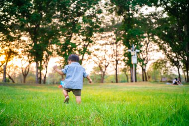 Neşeli çocuk Asyalı 2 yaşındaki çocuk şehir parkında oynuyor. Gün batımı sıcak hava aktivitesi.