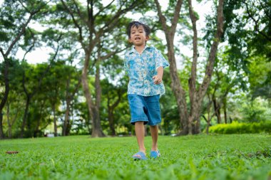 Asyalı anaokulu çocuğu şehir parkındaki yeşil tropikal ağaç ormanlarında geziyor.