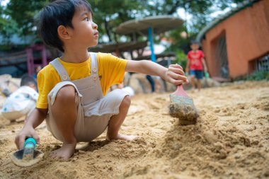 Asyalı çocuk. 5 yaşında. Kum havuzunda oyun oynuyor. Açık havada kreş aktiviteleri
