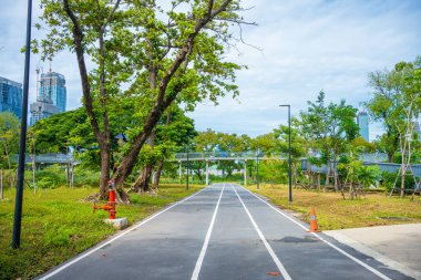 Asplalt, yeşil ağaç ormanı ve ofis yapım geçmişiyle birlikte şehir parkında yürüyüş yapıyor.