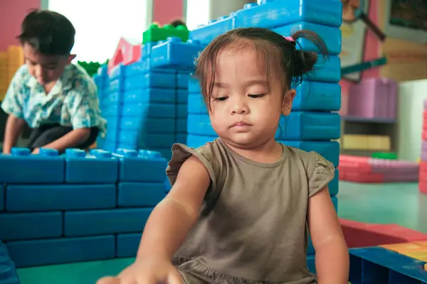 Adorable little girl enjoying with building toy block indoor playground happy preschool girl