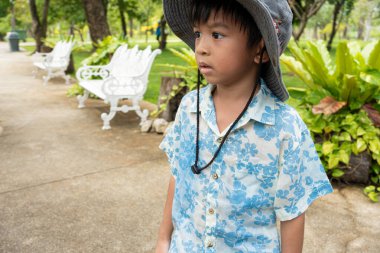 Asyalı anaokulu çocuğu şehir parkındaki yeşil tropikal ağaç ormanlarında geziyor.