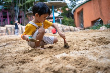 Asyalı çocuk. 5 yaşında. Kum havuzunda oyun oynuyor. Açık havada kreş aktiviteleri
