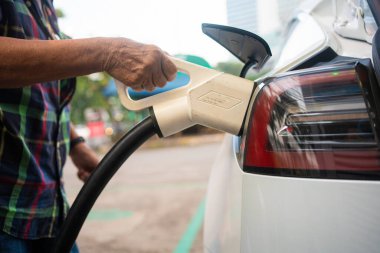 Asyalı olgun bir kadın elektrik kablosunu istasyonda tutuyor, çevre dostu sıfır emisyon.