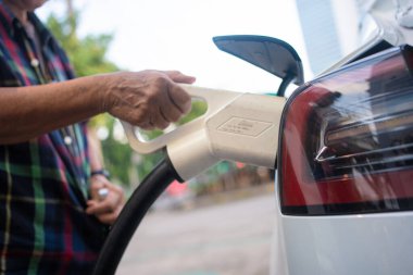 Asyalı olgun bir kadın elektrik kablosunu istasyonda tutuyor, çevre dostu sıfır emisyon.