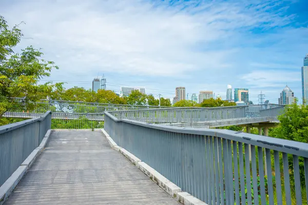 Asplalt, yeşil ağaç ormanı ve ofis binalarıyla şehir parkında yürüyüş yapıyor.  