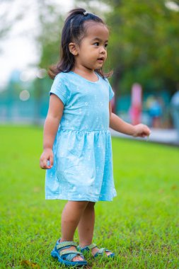 Mutlu Asyalı 2 yaşındaki kız şehir parkında yeşil çimlerin üzerinde gün batımının tadını çıkarıyor.