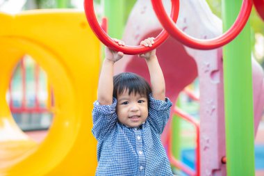 2-3 yaşlarında Asyalı bir çocuk oyun parkında bara tırmanıyor.