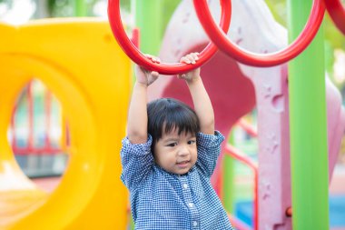 2-3 yaşlarında Asyalı bir çocuk oyun parkında bara tırmanıyor.