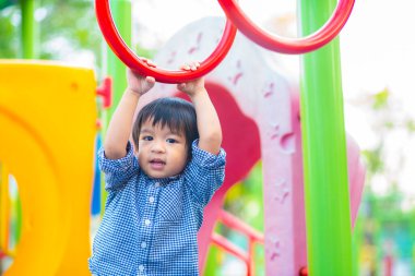 2-3 yaşlarında Asyalı bir çocuk oyun parkında bara tırmanıyor.