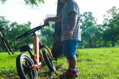 Okul öncesi Asyalı çocuk şehir parkında bisiklet sürme alıştırması yapıyor.