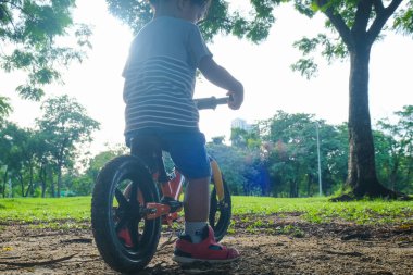 Okul öncesi Asyalı çocuk şehir parkında bisiklet sürme alıştırması yapıyor.