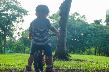 Okul öncesi Asyalı çocuk şehir parkında bisiklet sürme alıştırması yapıyor.