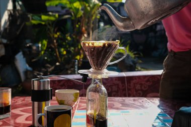 Evdeki açık havada sabah masasında filtrelenmiş yerel kahve demleyen bir adam.