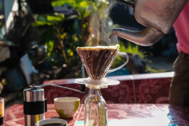 Evdeki açık havada sabah masasında filtrelenmiş yerel kahve demleyen bir adam.