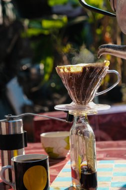 Evdeki açık havada sabah masasında filtrelenmiş yerel kahve demleyen bir adam.