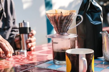 Evdeki açık havada sabah masasında filtrelenmiş yerel kahve demleyen bir adam.