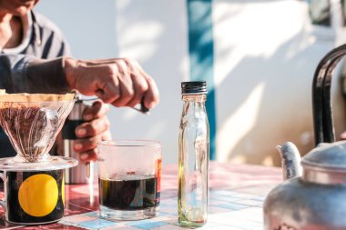 Evdeki açık havada sabah masasında filtrelenmiş yerel kahve demleyen bir adam.