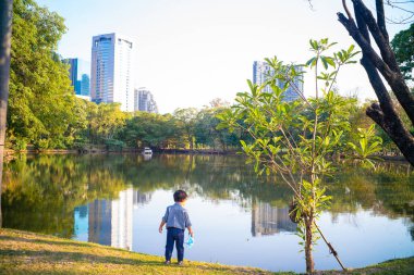 Asyalı çocuk şehir parkında oynuyor. Nehir kenarında, açık hava eğlencesi.