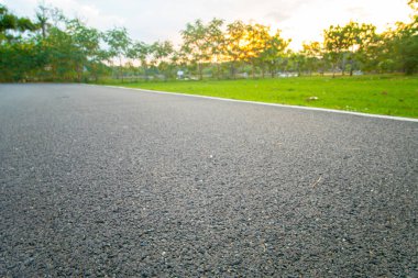 Asfalt yol parkı koşu yolu üzerinde gün batımı ışığı ve doğa arka planıyla yeşil çayır otları ile yol