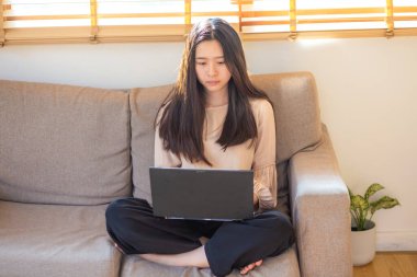 İş adamı Asyalı sıradan bir kadın dizüstü bilgisayarında rahat ofis bilgi teknolojisinde koltukta oturuyor.