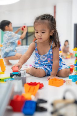 Sevimli anaokulu çocuğu Asyalı oğlan ve kız kapalı alanda renkli oyuncak bloğu eğitimi oynuyorlar.