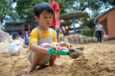 Asyalı çocuk. 5 yaşında. Kum havuzunda oyun oynuyor. Açık havada kreş aktiviteleri
