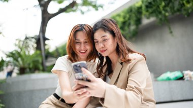 Mutlu Asyalı meslektaşlar iş günü dışarıda ofis binasında sosyal medya içeriğini araştırırken 5G kablosuz, komik kadın ortaklar internet bağlantısı kurarken hücresel uygulamayı tartışıyorlar.