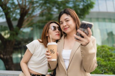 Mutlu Asyalı meslektaşlar iş günü dışarıda ofis binasında sosyal medya içeriğini araştırırken 5G kablosuz, komik kadın ortaklar internet bağlantısı kurarken hücresel uygulamayı tartışıyorlar.