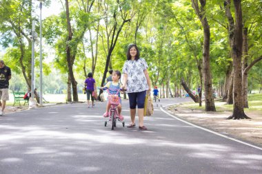 Asyalı kız bisikletle ağaç ormanlarında halka açık parkta güneşli bir günde spor yapıyor.