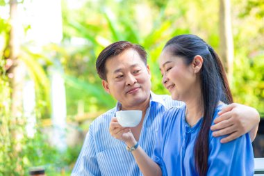 Asyalı son sınıf çifti sıcak kahve içerken ev bahçesinde otururken mutlu bir son sınıf aşkı hissediyorlar.