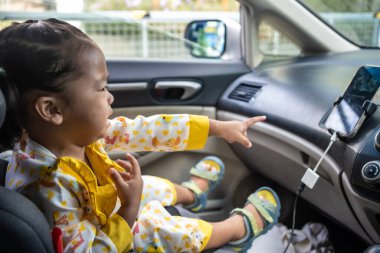 Küçük kız emniyet kemeriyle koltuğa oturmuş eğleniyor.