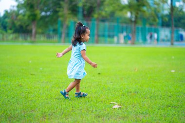 Sevimli küçük Asyalı kız yeşil çimlerde yürüyüp koşuyor. Gün batımında doğayla iç içe.