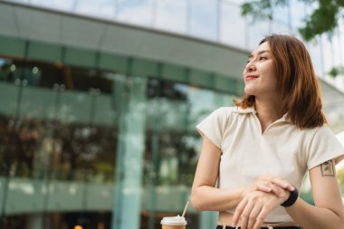 Asyalı iş kadını modern ofis binasında ayakta duran akıllı saati kullanıyor.