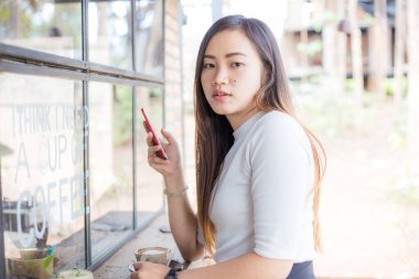 Güzel iş kadını Asyalı akıllı telefon iş iletişimini kullanıyor. Kahve dükkanında oturup dinleniyor.