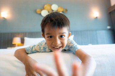 Küçük anaokulu çocuğu beyaz yastıklı otel odası seyahatinin tadını çıkarıyor.
