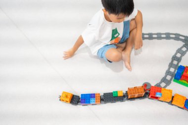 Sevimli Asyalı anaokulu çocuğu beyaz oda eğitimi konseptinde oyuncak tren bloğunda eğleniyor.