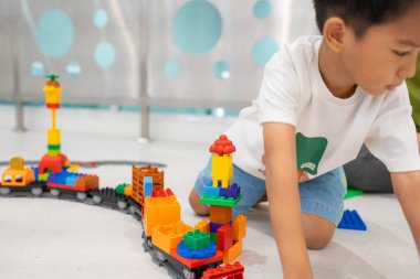 Sevimli Asyalı anaokulu çocuğu beyaz oda eğitimi konseptinde oyuncak tren bloğunda eğleniyor.