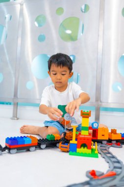 Sevimli Asyalı anaokulu çocuğu beyaz oda eğitimi konseptinde oyuncak tren bloğunda eğleniyor.