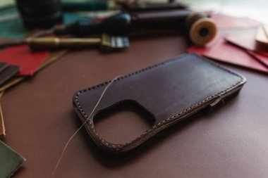 Deri arka plan üzerinde çalışan el yapımı hakiki deri telefon kılıfı ustalığı.