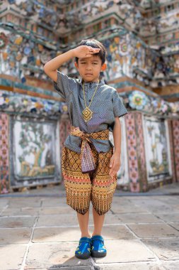 Anaokulu çocuğu geleneksel takım elbise giyer. Şafak vakti Budist tapınağı Wat Arun Bangkok Tayland 'a seyahat eder.