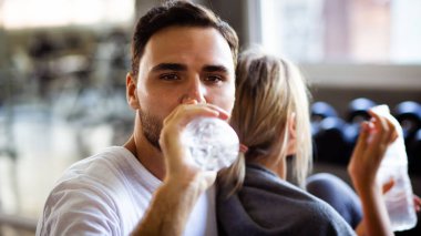 Spor salonundaki genç beyaz çift egzersizden sonra su içip sohbet ediyorlar. Sağlıklı aşk kavramı