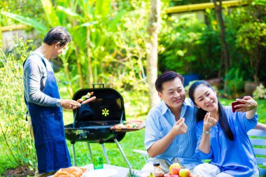 Park 'ta barbekü ızgara yemek partisi veren Asyalı mutlu bir arkadaş.